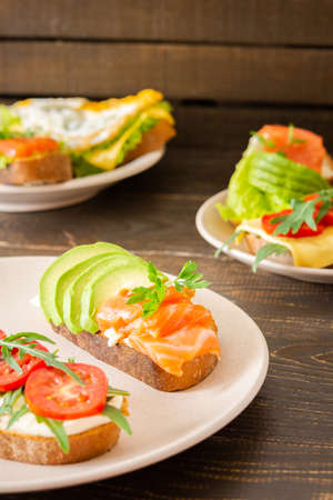 Different delicious sandwiches for breakfast, bread with cheese, avocado and trout, sandwich with egg, tomato and rucola, parsleyの写真素材