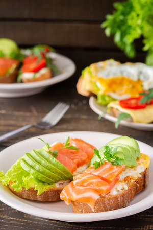 Different delicious sandwiches for breakfast, bread with cheese, avocado and trout, sandwich with egg, tomato and rucola, parsleyの写真素材
