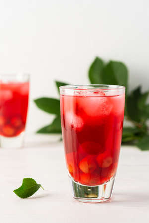 Summer delicious refreshing cherry compote with pulp and with ice in glasses on a white backgroundの写真素材