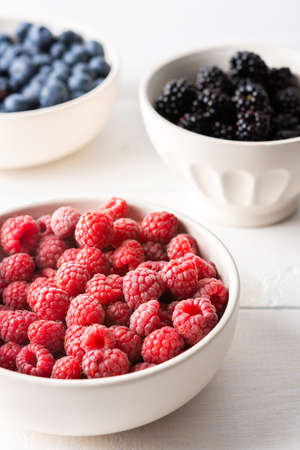 Raspberries, blueberries and blackberries close-up in bowls on a white background, ripe juicy berriesの写真素材