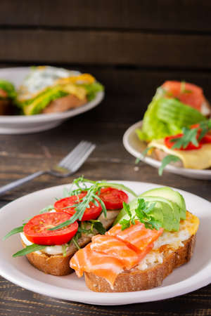 Different delicious sandwiches for breakfast, bread with cheese, avocado and trout, sandwich with egg, tomato and rucola, parsleyの写真素材