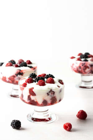 Delicious juicy berries of raspberries and blackberries with yoghurt in a glass form on a white backgroundの写真素材