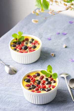 Delicious clafoutis made from white yogurt and berries, raspberries and blueberries, clafoutis in portioned bowls on the tableの写真素材