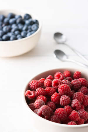 Raspberries and blueberries close-up in bowls on a white background, ripe juicy berriesの写真素材