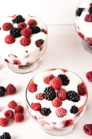 Delicious juicy berries of raspberries and blackberries with yoghurt in a glass form on a white backgroundの写真素材