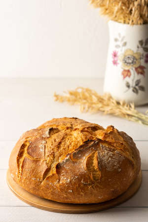 Loaf of homemade bread from wheat and seeds on the kitchen board , ears in a jugの写真素材
