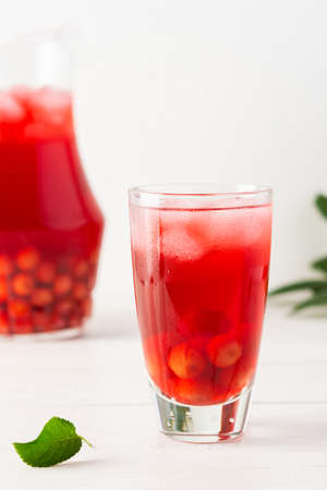 Summer delicious refreshing compote of cherries with pulp and with ice in glasses on a white background, a jug with a drinkの写真素材
