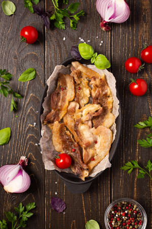 Fried pork bacon in a cast iron pan with tomatoes and spices and onionsの写真素材