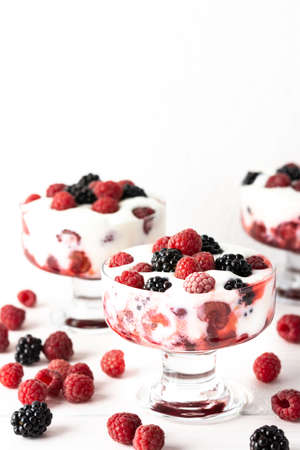 Delicious juicy berries of raspberries and blackberries with yoghurt in a glass form on a white backgroundの写真素材
