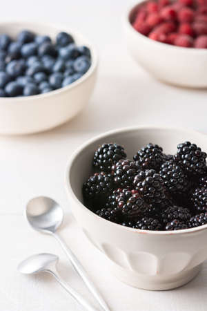 Raspberries, blueberries and blackberries close-up in bowls on a white background, ripe juicy berriesの写真素材
