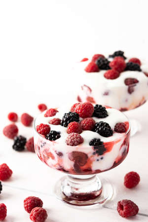 Delicious juicy berries of raspberries and blackberries with yoghurt in a glass form on a white backgroundの写真素材