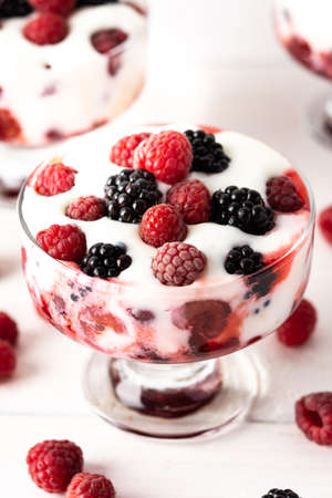 Delicious juicy berries of raspberries and blackberries with yoghurt in a glass form on a white backgroundの写真素材
