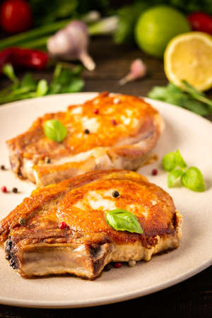 Fried pork entrecote on the bone, cooked pieces of pork meat with basil leaves and spices, steak on the bone in a plate on a wooden backgroundの写真素材