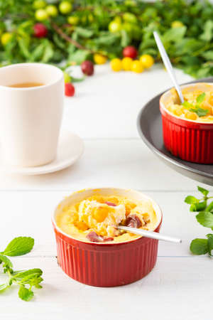 Delicious clafoutis made from white yogurt and berries, cherry plum dessert in portioned bowls on the table with a cup of juiceの写真素材