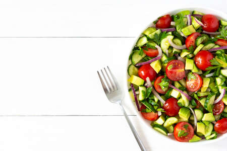 Salad of fresh ripe tomato, onion, avocado, cucumber and parsley and olive oil, salad in a white plate with a fork and towel on a white wooden backgroundの写真素材