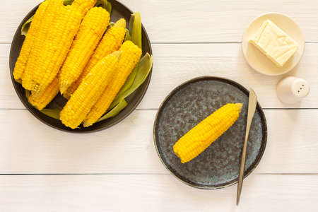 Delicious juicy sweet boiled corn in a plate on a white wooden background, cooked corn cobs with butter and saltの写真素材