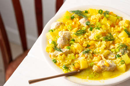 Delicious hearty lunch, soup with chicken and rice, young corn ,green onions and potato in a plate on the tableの写真素材