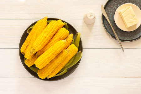 Delicious juicy sweet boiled corn in a plate on a white wooden background, cooked corn cobs with butter and saltの写真素材