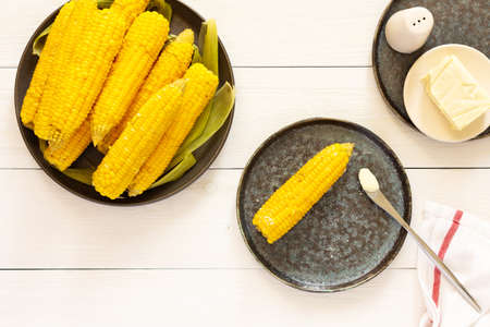 Delicious juicy sweet boiled corn in a plate on a white wooden background, cooked corn cobs with butter and saltの写真素材