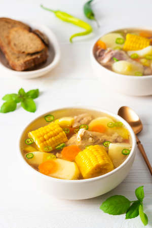 Delicious hearty lunch, soup with chicken and rice, sweet boiled corn ,green onions and potato in a plate on the table with bread, beautiful bouquet of flowers in a vaseの写真素材