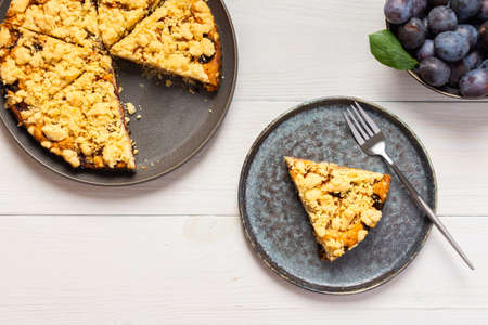 Delicious juicy dessert on a white wooden background, portions of plum pie in a plate with a forkの写真素材