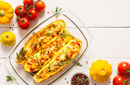 Stewed yellow zucchini with tomatoes and onions, cheese and herbs, carrots and spices, stuffed zucchini on a white wooden backgroundの写真素材