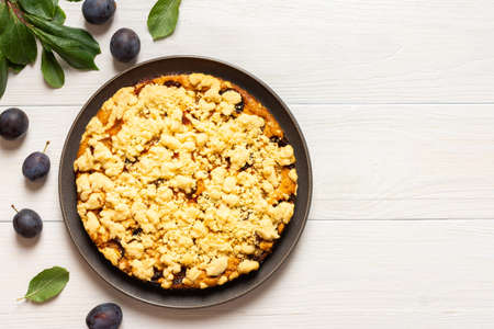 Delicious juicy plum cake in a round plate on a white wooden background, plum tree leaves with fruitsの写真素材