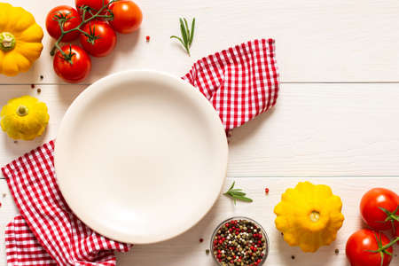 White wooden background with empty plate and ingredients, tomatoes and rosemary, pattypan squash and spices , top viewの写真素材