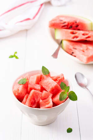 Juicy ripe sweet red watermelon slices with mint leaves in a bowl on a white background, delicious summer berriesの写真素材