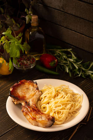 Fried pork entrecote on the bone and pasta in a plate on a wooden background, cooked pieces of pork meat with basil leaves and spices, steak on the boneの写真素材