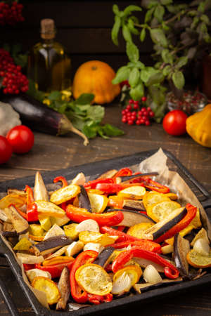 Baked vegetables in the oven, eggplant and zucchini, bell peppers and onions with spices, vegetables on a baking sheet on a wooden backgroundの写真素材