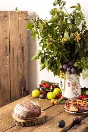 Blueberry and plum bread on a wooden background, berries and fruits on the table, plum branches in a vase, rustic interiorの写真素材