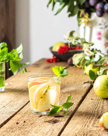 Autumn apple drink, apple slices with juice and mint in a glass on a wooden table, leaves in a vase, morning in the village, rustic conceptの写真素材