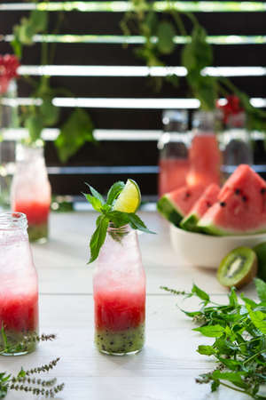 Cold refreshing watermelon juice, watermelon with kiwi and ice in bottles, fruit smoothie on wooden backgroundの写真素材