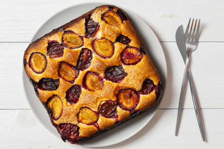 Delicious juicy plum pie in a round plate on a white wooden background, square cake, top viewの写真素材