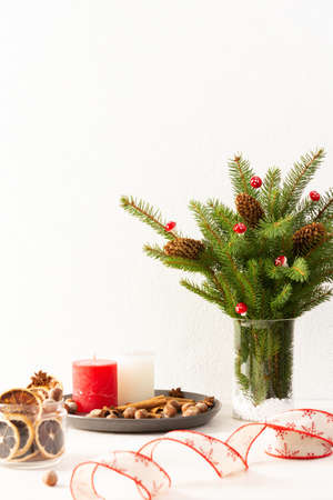 Candles with dried slices of citrus fruits, hazelnuts with cinnamon, fir tree branches and cones in a vase on white wall background, new year and christmas conceptの写真素材