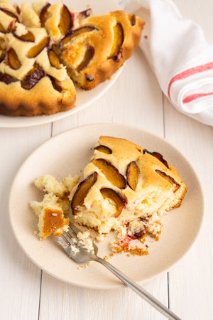 Delicious juicy dessert on a white wooden background, portions of plum pie in a plate with a fork