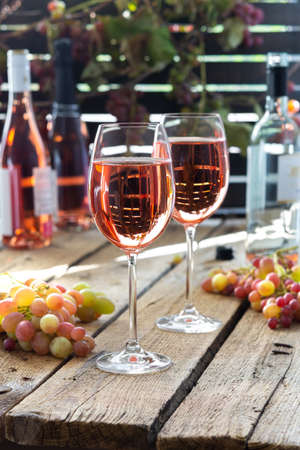 Full glasses of rose wine, outdoor recreation, wooden table with glasses of wine, bottles of wine and grapesの写真素材