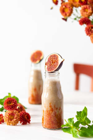 Delicious fresh healthy fruit smoothie in glass jars, fig with melon and banana, autumn chrysanthemum flowers with mintの写真素材