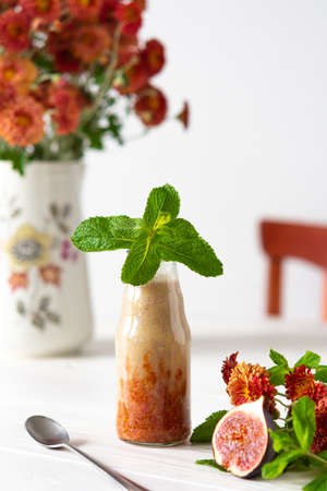 Delicious fresh healthy fruit smoothie in glass jars, fig with melon and banana, autumn chrysanthemum flowers with mintの写真素材