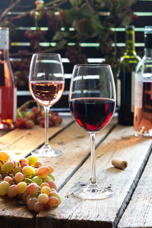 Glasses with red and rose wine, outdoor recreation, wooden table with glasses of wine, bottles of wine and grapesの写真素材