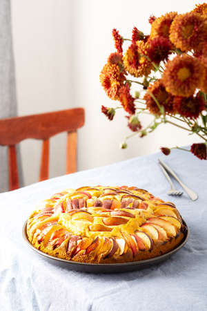 Delicious apple pie, home interior, table with blue tablecloth, vase with autumn flowers chrysanthemumsの写真素材