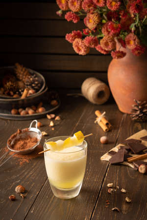 Refreshing delicious melon smoothie with cinnamon, hazelnuts and chocolate, vase of chrysanthemums and glasses of smoothie on wooden backgroundの写真素材