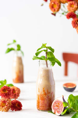 Delicious fresh healthy fruit smoothie in glass jars, fig with melon and banana, autumn chrysanthemum flowers with mintの写真素材