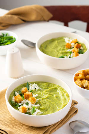 Healthy delicious broccoli and cucumber cream puree soup with mozzarella, green onions and croutons, bowl of soup on a white tableの写真素材