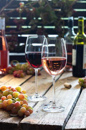 Glasses with red and rose wine, outdoor recreation, wooden table with glasses of wine, bottles of wine and grapesの写真素材