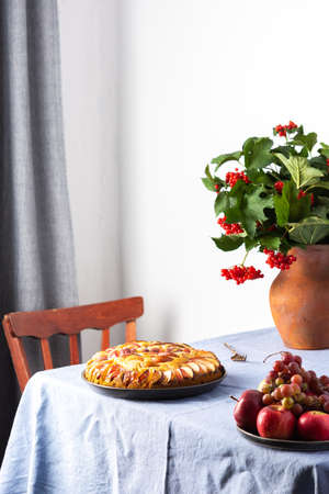 Delicious apple pie, home interior, table with blue tablecloth, vase with autumn flowers chrysanthemumsの写真素材