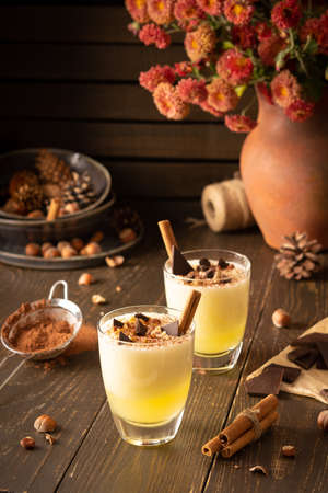 Refreshing delicious melon smoothie with cinnamon, hazelnuts and chocolate, vase of chrysanthemums and glasses of smoothie on wooden backgroundの写真素材