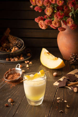Refreshing delicious melon smoothie with cinnamon, hazelnuts and chocolate, vase of chrysanthemums and glasses of smoothie on wooden backgroundの写真素材