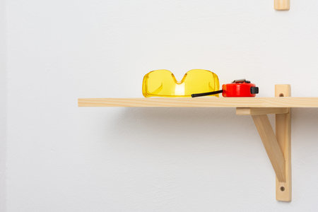The process of fixing a wooden shelf to the wall, goggles and a tape measure lie on the attached...